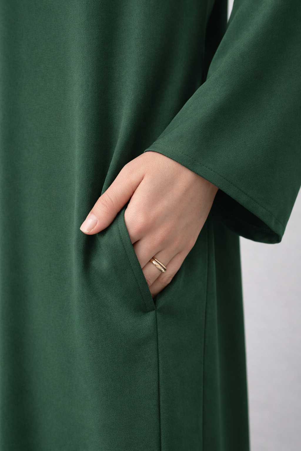 Green coat with a hand reaching into the pocket against a neutral background