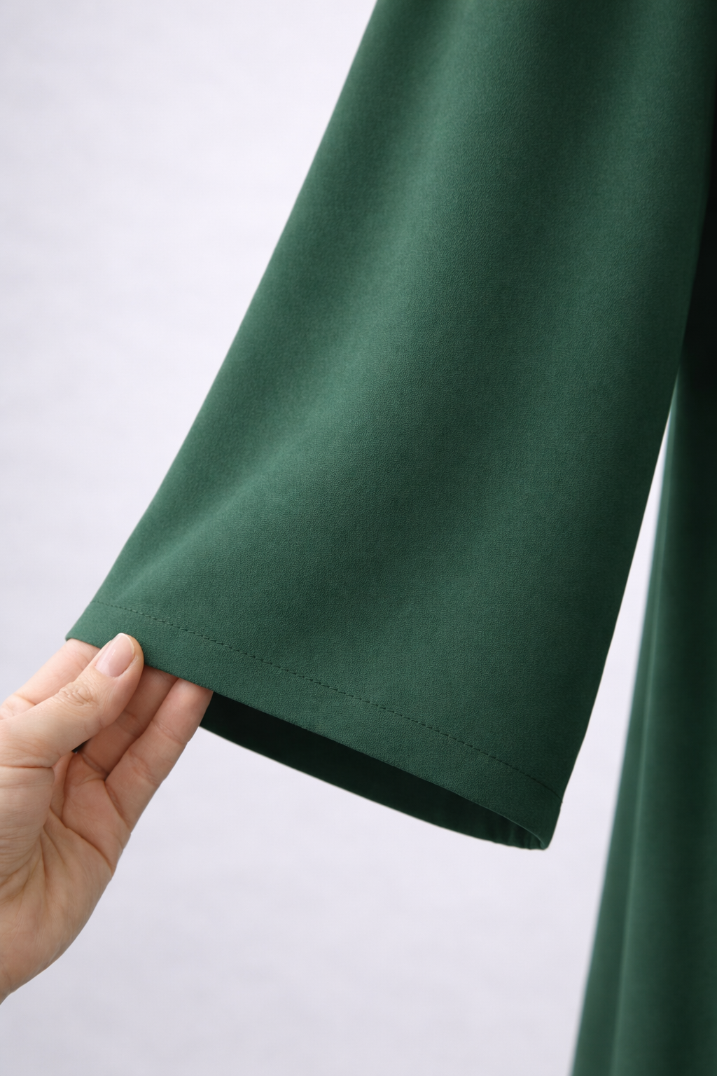 Green fabric held by a hand against a light gray background