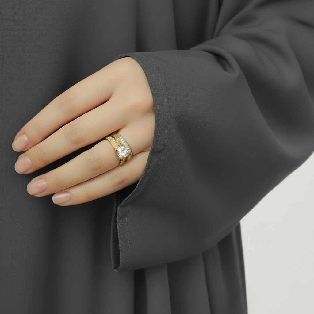 Abaya sleeve and hand wearing a gold ring with a diamond on a plain background